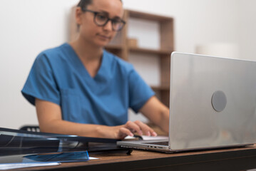 Lady doctor in glasses works on laptop sitting at desk practitioner communicates with patient...