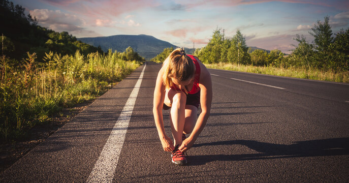Fitness blonde woman running on the asphalt road at the mountains