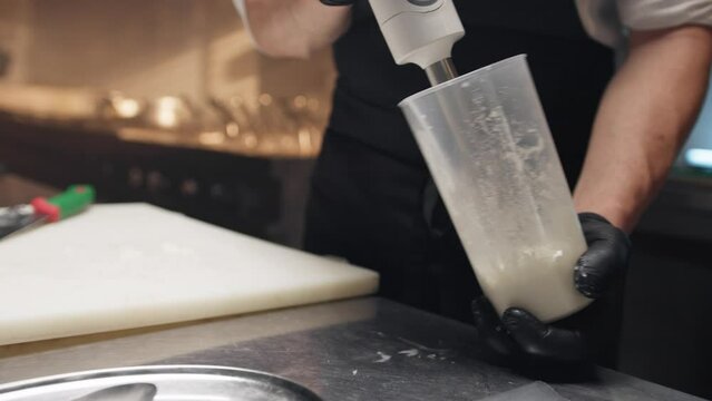 Cook uses immersion mixer blender to prepare a sauce