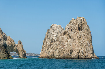 Mexico, Cabo San Lucas - July 16, 2023: South view on Reserva de Los Marina, El Arco and channel between tall gray boulders in greenish ocean water. Cityscape and beach on horizon