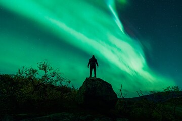 A silhouette of young adventurous male traveller watching the northern lights also known as aurora...