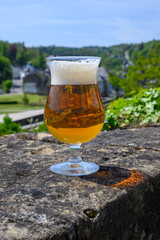 Glass of blond strong Belgian abbey beer on old castle wall in sunny day with nice view on old town...