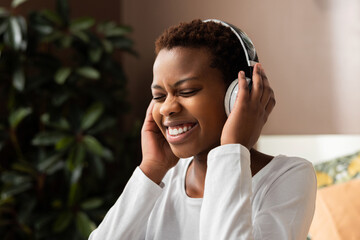 Happy adorable american woman in whote shirt singing and having fun while listening to music using wireless earphones at home day off concept at weekends