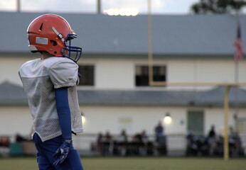 Kid football player waiting his turn, orange hamlet, white and blue uniform.