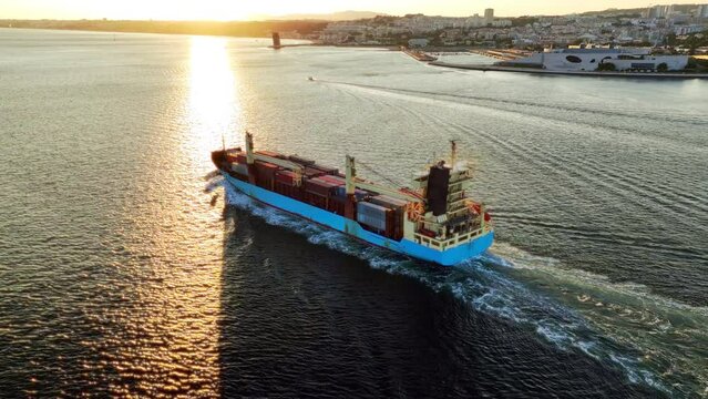 Aerial drone view of Tagus River with cargo container ship leaving Lisbon port at sunset. Lisbon, Portugal. Orbit parallax shot