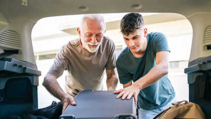 Two men Teenager and senior grandfather pack baggage in trunk of car