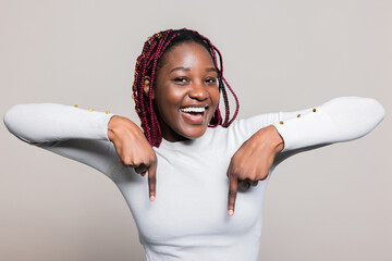 Happy cheerful attractive African American dark skinned woman with braids pointing down with index fingers banner concept copy space advertisemnt time