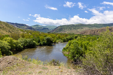 Fototapeta premium Mtkvari river valley landscape in Samtskhe Javakheti region in Southern Georgia with lush green vegetation and Lesser Caucasus mountains in the background.