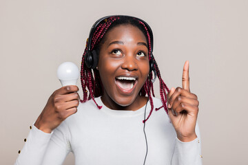 Alluring charming African American millennial woman with colorful braids is holding a lightbulb in...