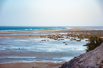 Landscape of Sotavento beach in Fuerteventura with blue water and white sand with some bushes and some puddles of water with a clear blue sky.