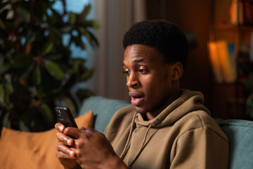 Shocked surprised African American dark skinned black avid gamer playing his favorite mobile game feeling immersed in the virtual world