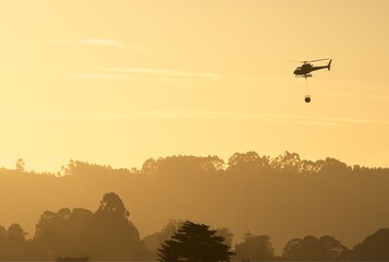 Emergency helicopter, firefighters, with the last hours of the setting sun heading to a fire in the mountains.
