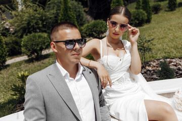 Cool bride and groom having fun and wearing sunglasses outdoors in sunny weather