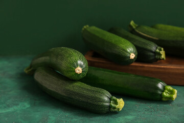Wooden board with many fresh zucchini on green table