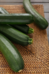 Wicker mat with many fresh zucchini on black wooden background