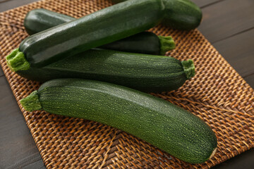 Wicker mat with many fresh zucchini on black wooden background
