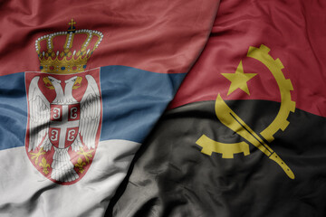 big waving national colorful flag of serbia and national flag of angola .