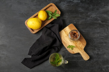 Wooden boards with cup of fresh mint tea, lemons and cinnamon on grunge black background