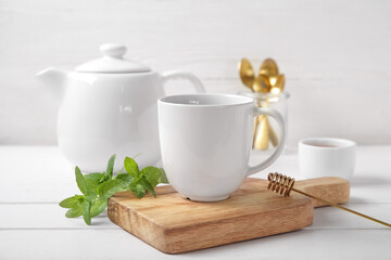 Teapot with cup of fresh mint tea, honey and spoons on white wooden table