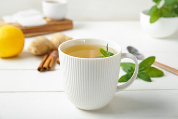 Cup of fresh mint tea with lemon, ginger root and cinnamon on white wooden table
