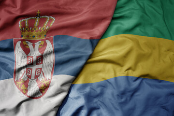 big waving national colorful flag of serbia and national flag of gabon .