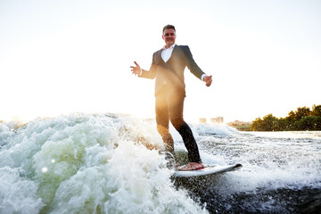 Young man in classic suit rides a wakeboard on the river or lake near city. Clerk escaped from a...