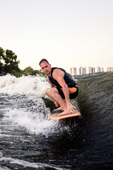 Fototapeta premium Young athletic man energetically riding wakeboard. Handsome caucasian guy glides on the wave like a real surfer. Active lifestyle and extreme sports. Summertime watersports activity.