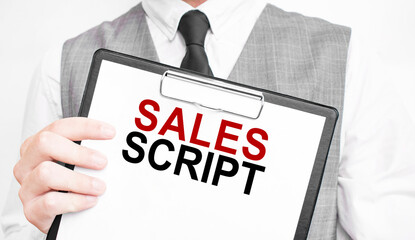 SALES SCRIPT inscription on a notebook in the hands of a businessman on a gray background, a man...
