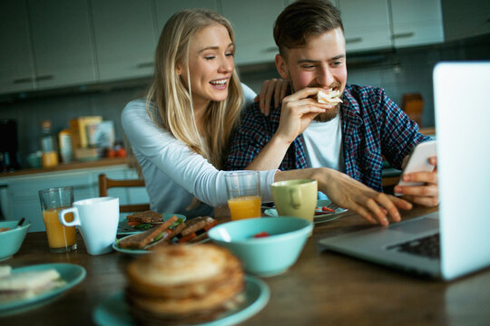 Young Caucasian couple using a smartphone while having breakfast in the kitchen