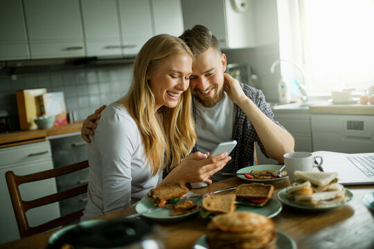 Young Caucasian couple using a smartphone while having breakfast in the kitchen