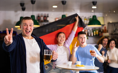 Smiling man and woman with Germany flag drinking alcohol and having conversation on party in...