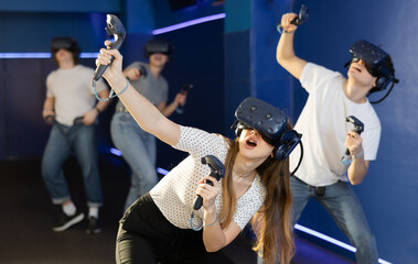 indoors, girl in virtual reality headset with joysticks in her hands actively moves and...
