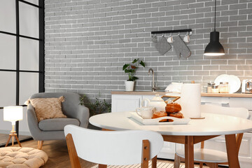 Interior of modern kitchen with glowing lamps, dining table, white counters and grey armchair at...