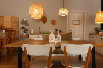 Interior of modern kitchen with glowing lamps, dining table and chairs at evening