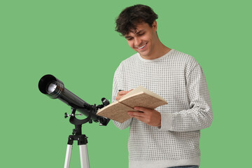 Young man with telescope and notebook on green background