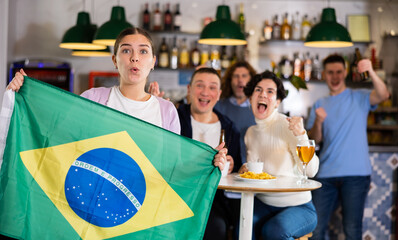 Emotional friends, football fans cheering for favorite Brazil team together while watching match on...