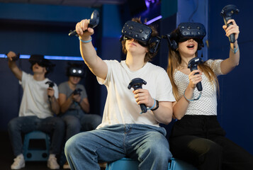 Excited modern young couple with gaming controllers in hands and VR goggles having fun with friends...