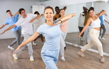 Active women and men dancing synchronous group choreography in dance hall