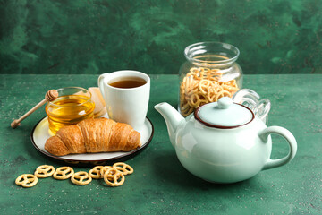 Composition with cup of tea, teapot, snacks and croissant on green table