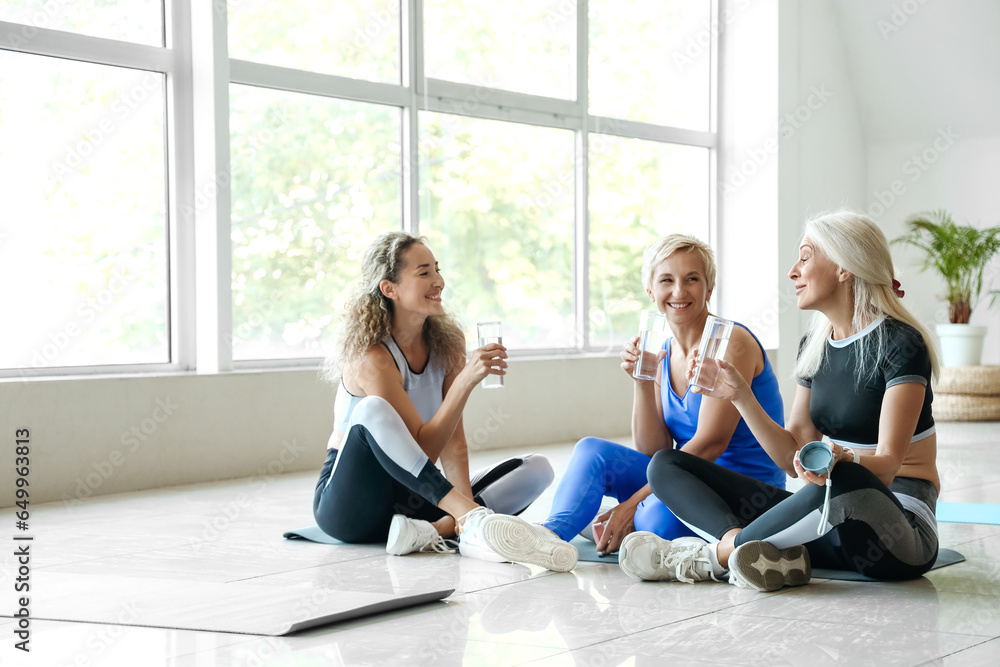Wall mural sporty mature women drinking water after practicing yoga in gym - Wall murals