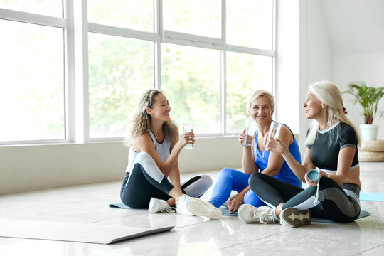 Sporty mature women drinking water after practicing yoga in gym
