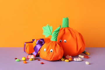 Paper pumpkins for Halloween, gift boxes and tasty candies on color background