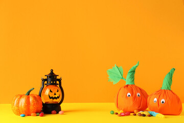 Paper pumpkins for Halloween, lantern and tasty candies on color background