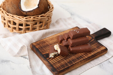 Wooden board with tasty chocolate covered coconut candies on white background
