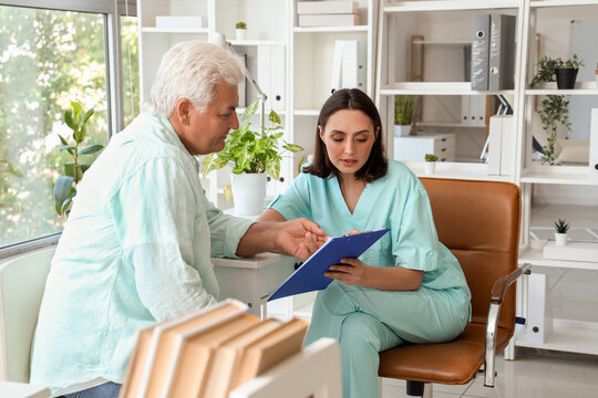 Female doctor showing something on clipboard to senior patient in medical office