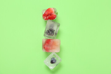 Frozen berries in ice cubes on green background