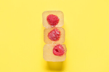 Frozen raspberries in ice cubes on yellow background