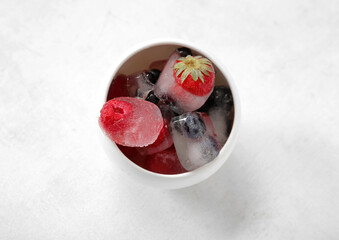 Bowl with frozen berries in ice cubes on white background