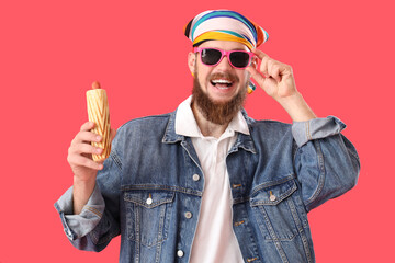 Portrait of fashionable young man with tasty hot dog on red background
