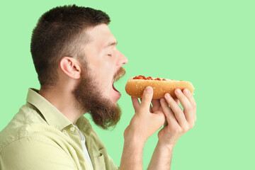 Portrait of handsome young man eating tasty hot dog on green background